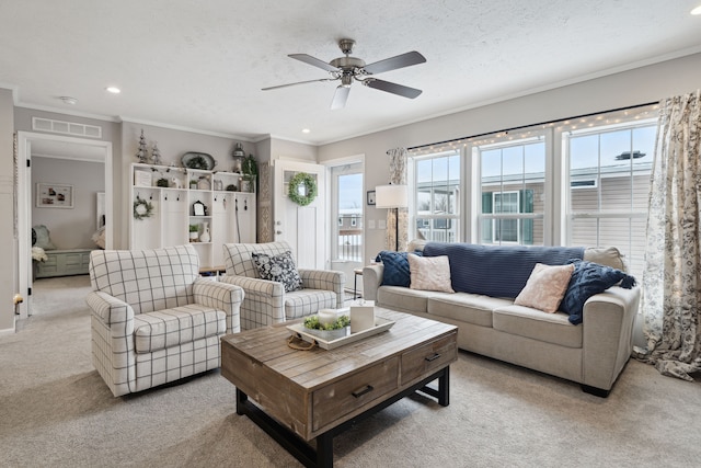 living room featuring ceiling fan, light colored carpet, ornamental molding, and a textured ceiling