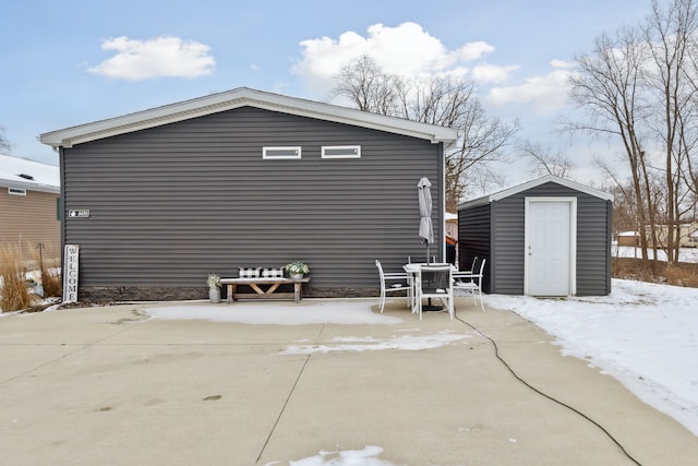 snow covered house with a storage unit and a patio area