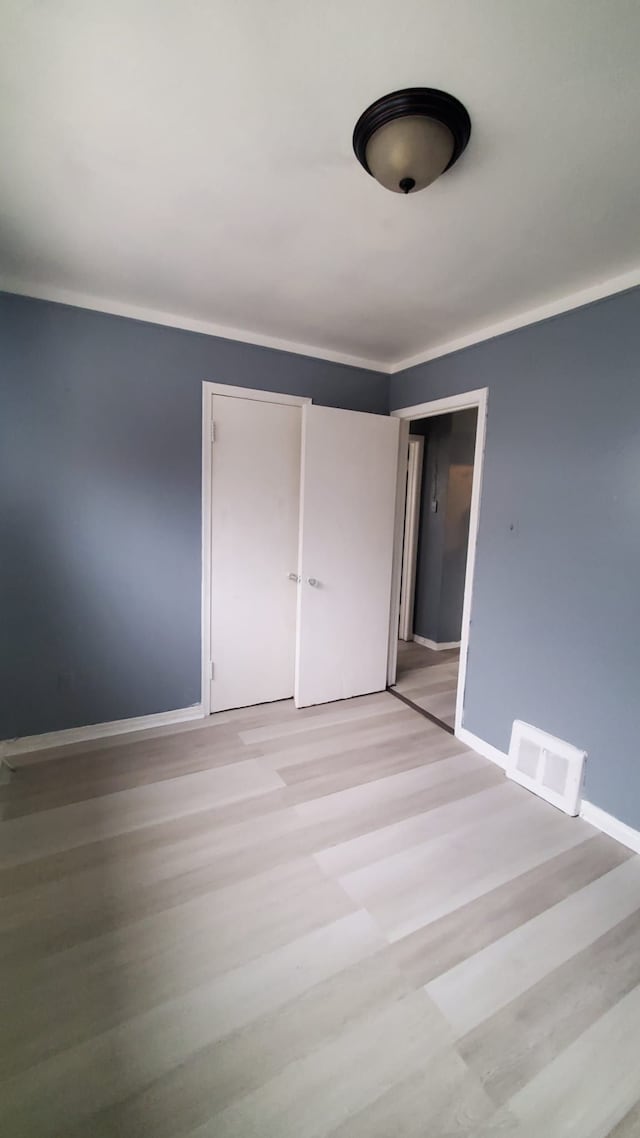 unfurnished bedroom featuring light hardwood / wood-style flooring, a closet, and crown molding