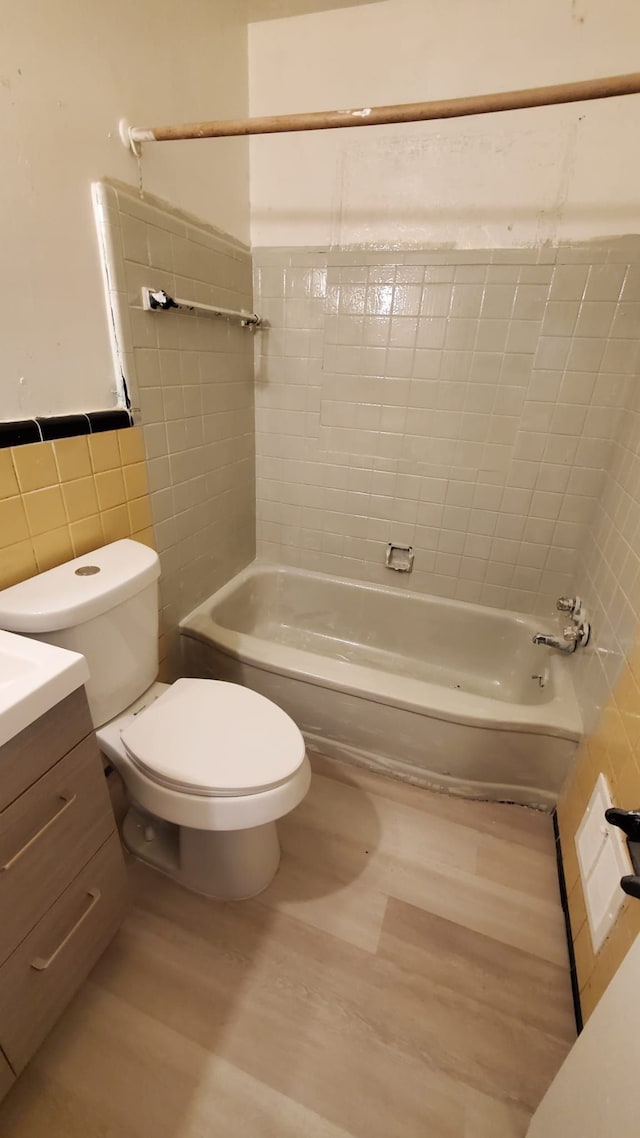 full bathroom featuring hardwood / wood-style floors, vanity, tiled shower / bath, toilet, and tile walls