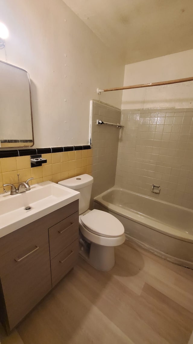 full bathroom with hardwood / wood-style floors, vanity, tiled shower / bath combo, toilet, and tile walls