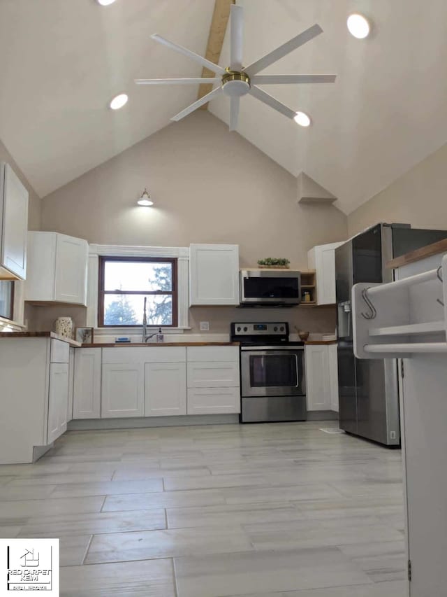 kitchen with high vaulted ceiling, stainless steel appliances, white cabinetry, and ceiling fan