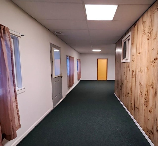 hallway featuring a drop ceiling, carpet, and wood walls