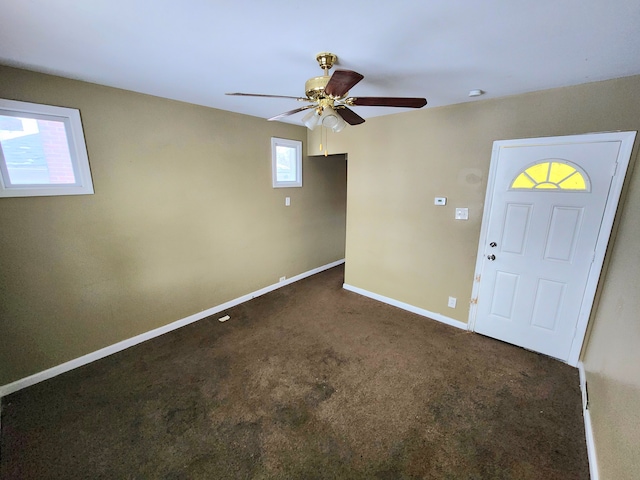 foyer entrance featuring ceiling fan and dark carpet