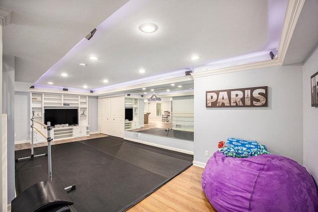 exercise room with wood-type flooring, a tray ceiling, built in features, and crown molding