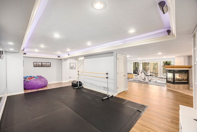 exercise room with hardwood / wood-style floors, a multi sided fireplace, and a raised ceiling