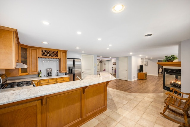 kitchen featuring light stone countertops, a multi sided fireplace, stainless steel fridge with ice dispenser, a breakfast bar, and range