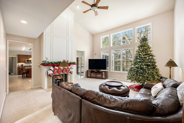 living room featuring a high ceiling, light colored carpet, ceiling fan, and a tiled fireplace