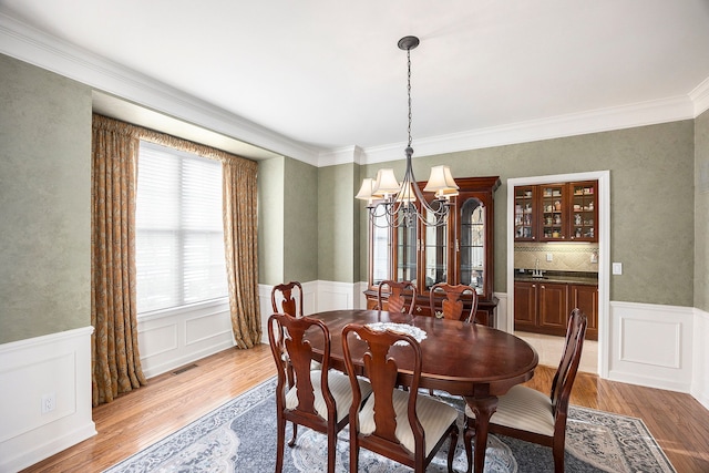 dining space featuring crown molding, light wood-style flooring, an inviting chandelier, and wainscoting