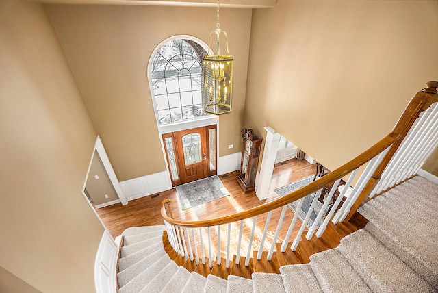 entryway featuring a towering ceiling, baseboards, a wainscoted wall, stairs, and wood finished floors