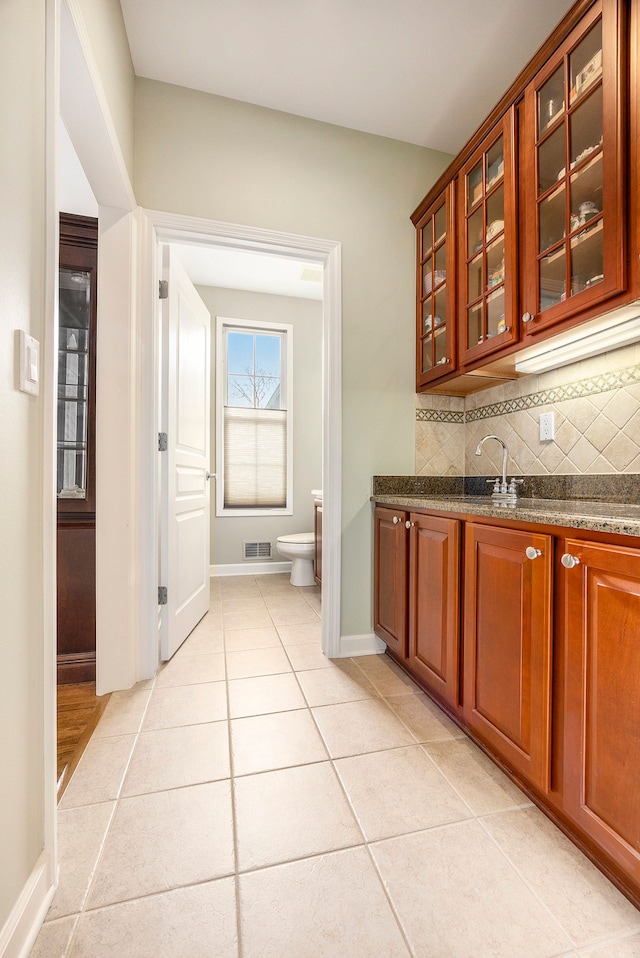 kitchen featuring tasteful backsplash, sink, light tile patterned floors, and dark stone counters