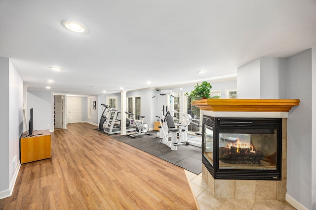 exercise room with a multi sided fireplace and light hardwood / wood-style flooring