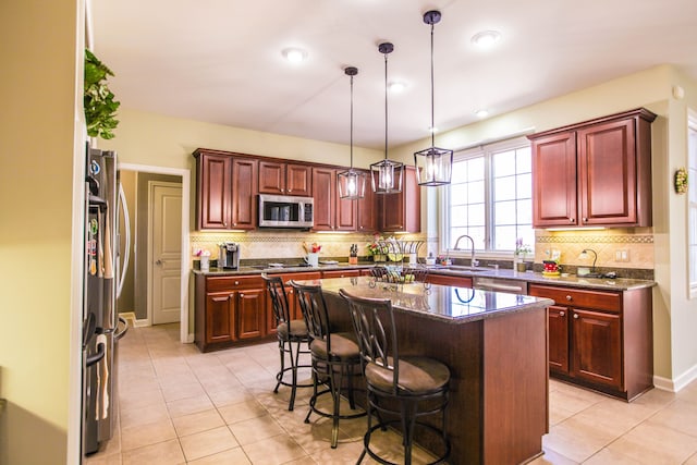 kitchen with appliances with stainless steel finishes, light tile patterned flooring, dark brown cabinets, and hanging light fixtures