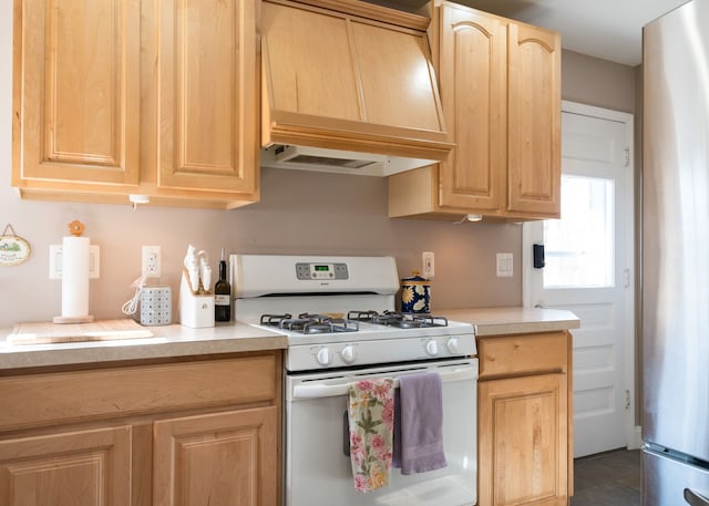 kitchen with light brown cabinets, stainless steel refrigerator, premium range hood, and white range with gas cooktop