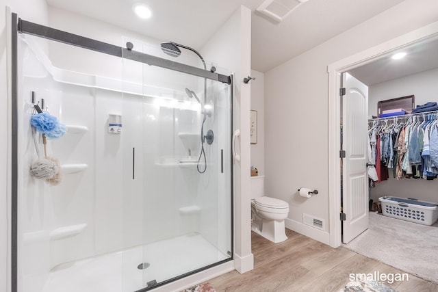 bathroom featuring toilet, wood-type flooring, and a shower with door