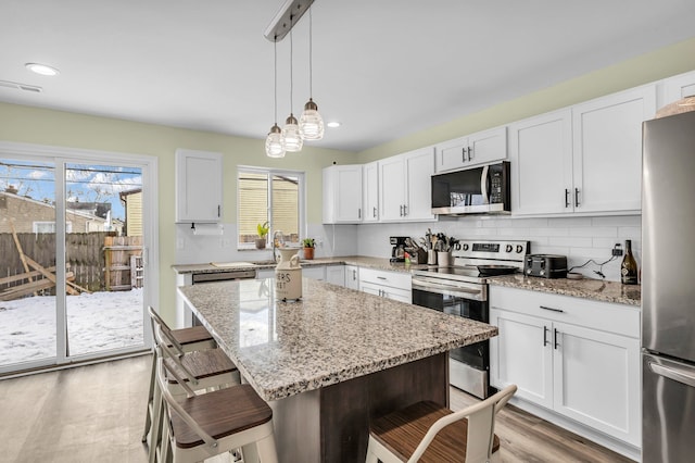 kitchen featuring white cabinets, appliances with stainless steel finishes, a center island, hanging light fixtures, and a breakfast bar