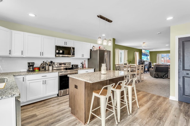 kitchen featuring light stone countertops, white cabinets, stainless steel appliances, and a kitchen island