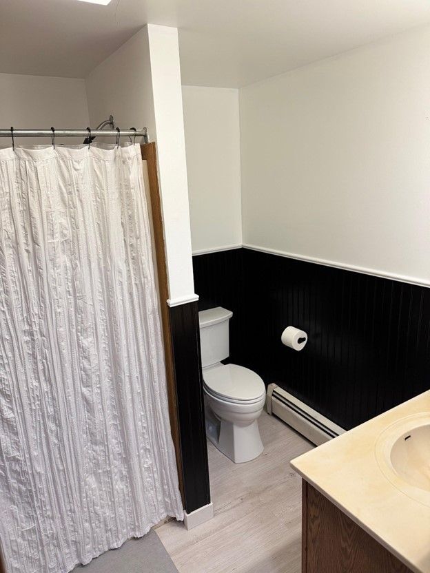 bathroom featuring toilet, a baseboard heating unit, wainscoting, vanity, and wood finished floors