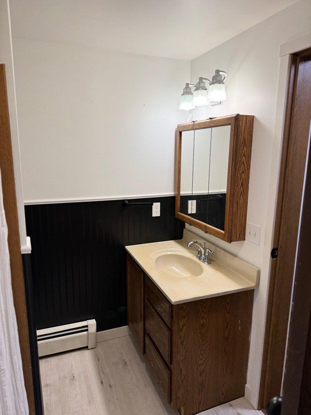 bathroom featuring wooden walls, a wainscoted wall, wood finished floors, vanity, and a baseboard heating unit