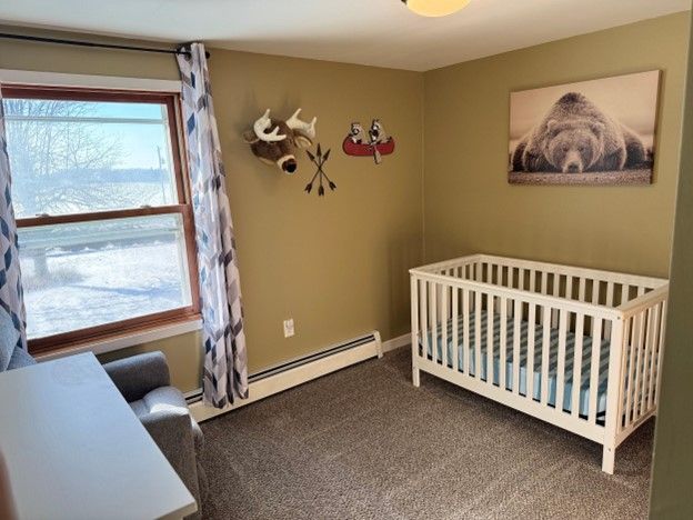 carpeted bedroom featuring a nursery area and a baseboard heating unit