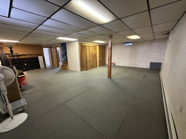 finished basement with stairs, baseboard heating, and a paneled ceiling