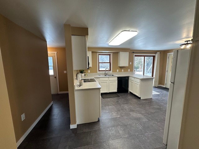 kitchen featuring a peninsula, a sink, black dishwasher, light countertops, and freestanding refrigerator