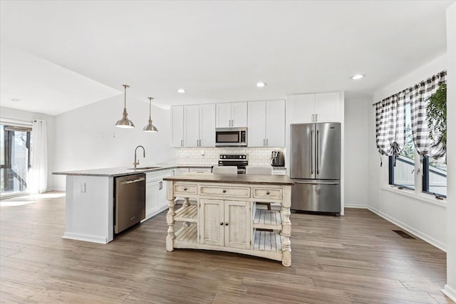 kitchen with a center island, sink, hanging light fixtures, appliances with stainless steel finishes, and a healthy amount of sunlight