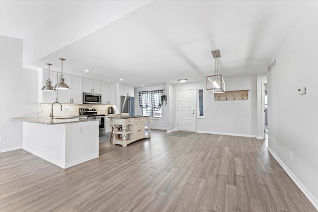 kitchen featuring kitchen peninsula, stainless steel appliances, sink, pendant lighting, and white cabinetry