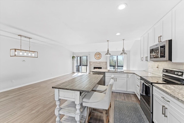 kitchen with tasteful backsplash, white cabinets, hanging light fixtures, and appliances with stainless steel finishes