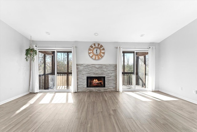 unfurnished living room featuring a stone fireplace, a wealth of natural light, and light hardwood / wood-style flooring