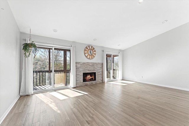 unfurnished living room featuring a stone fireplace, a wealth of natural light, and light hardwood / wood-style flooring