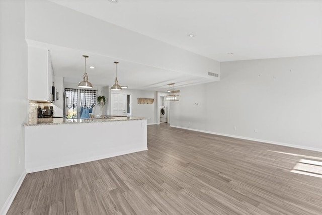 kitchen featuring white cabinetry, light stone countertops, hanging light fixtures, light hardwood / wood-style flooring, and kitchen peninsula