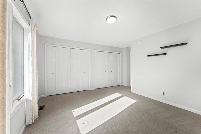 unfurnished bedroom featuring two closets, multiple windows, and light colored carpet