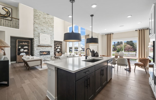 kitchen featuring a stone fireplace, sink, wood-type flooring, decorative light fixtures, and a center island with sink