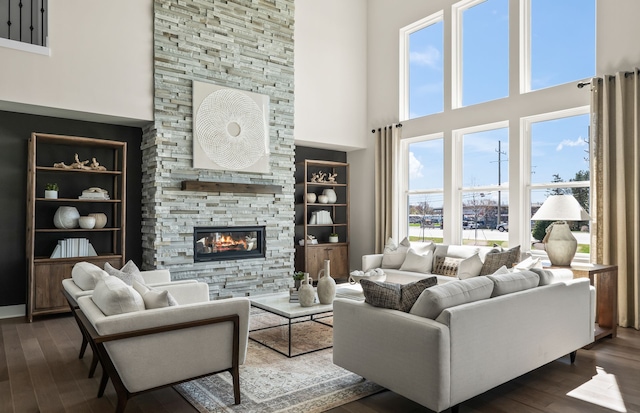 living room featuring dark hardwood / wood-style flooring, a stone fireplace, built in shelves, and a high ceiling