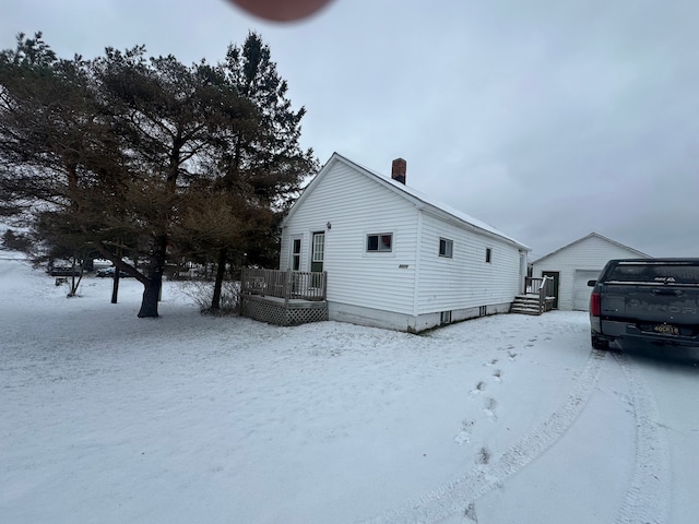 view of snowy exterior featuring an outbuilding, a garage, and a wooden deck