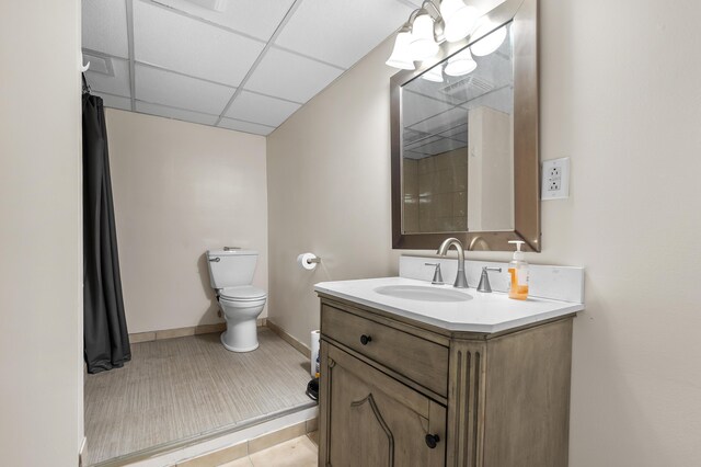 bathroom with tile patterned flooring, a paneled ceiling, toilet, and vanity