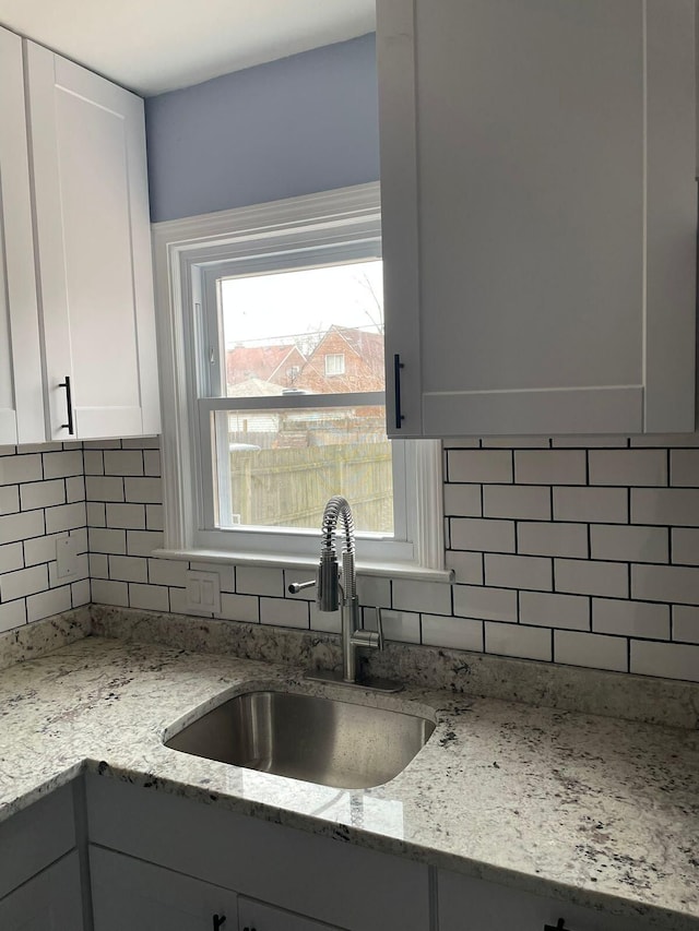 kitchen featuring light stone countertops, white cabinets, tasteful backsplash, and sink