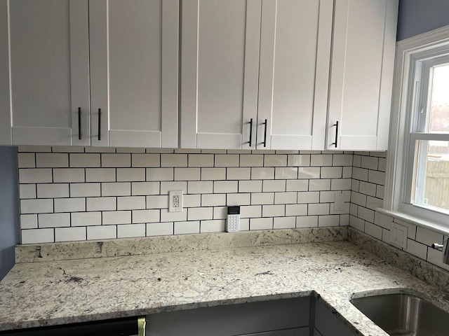 room details featuring white cabinetry, light stone countertops, sink, and tasteful backsplash