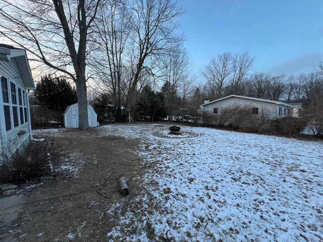 yard layered in snow with a fire pit and a shed