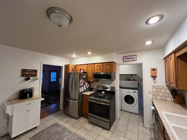 kitchen with decorative backsplash, washer / dryer, appliances with stainless steel finishes, light tile patterned flooring, and sink