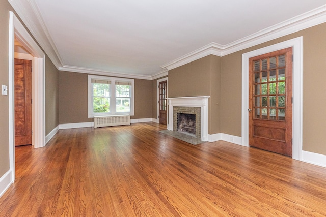 unfurnished living room with hardwood / wood-style floors, ornamental molding, radiator, and a brick fireplace