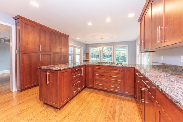 kitchen with kitchen peninsula, pendant lighting, an inviting chandelier, stone counters, and light hardwood / wood-style floors