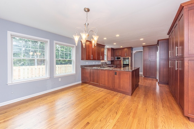 kitchen featuring dark stone counters, hanging light fixtures, light hardwood / wood-style flooring, stainless steel appliances, and a chandelier