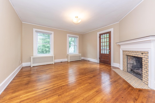 unfurnished living room with radiator heating unit, a brick fireplace, crown molding, and wood-type flooring