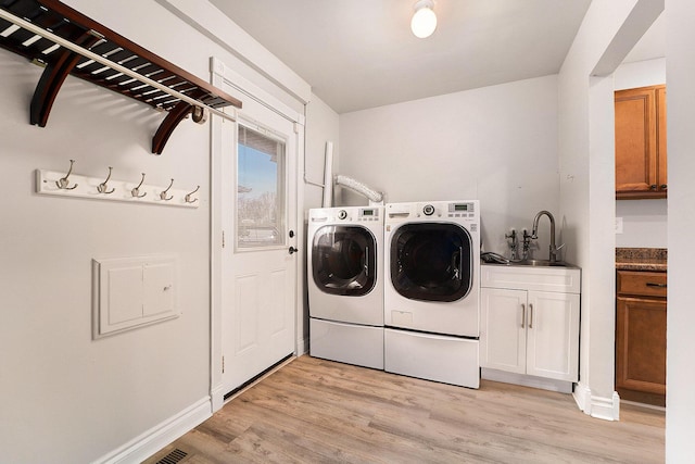 washroom featuring washing machine and clothes dryer, sink, cabinets, and light wood-type flooring