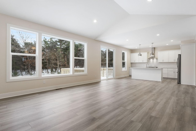 unfurnished living room with light wood-type flooring, lofted ceiling, and a wealth of natural light