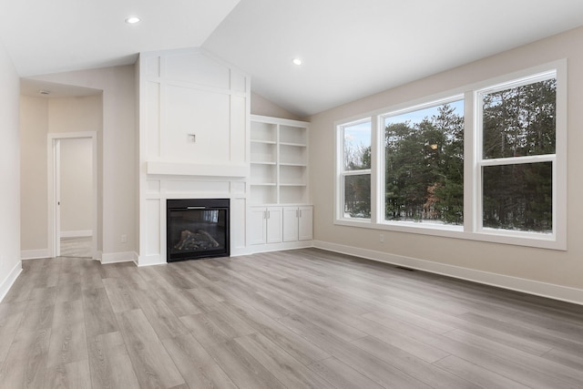 unfurnished living room featuring built in shelves, a large fireplace, lofted ceiling, and light hardwood / wood-style flooring