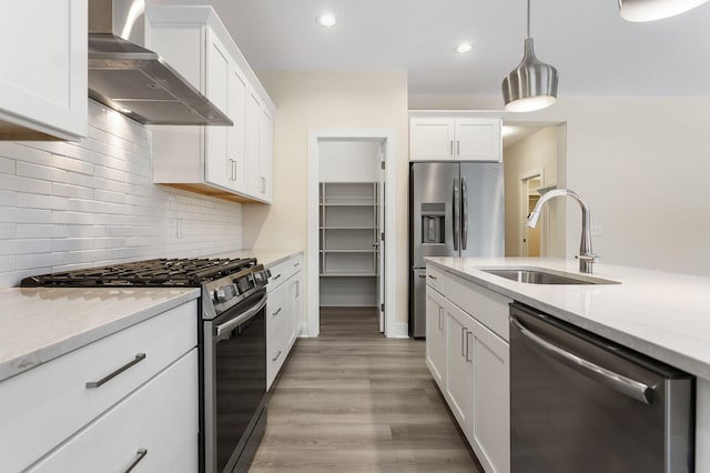 kitchen featuring appliances with stainless steel finishes, sink, wall chimney range hood, pendant lighting, and white cabinetry