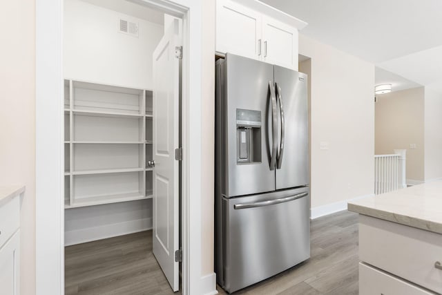 kitchen featuring light stone countertops, light hardwood / wood-style flooring, white cabinets, and stainless steel refrigerator with ice dispenser